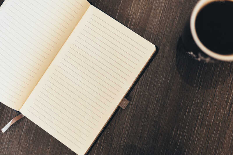 An open lined notebook beside a cup of coffee