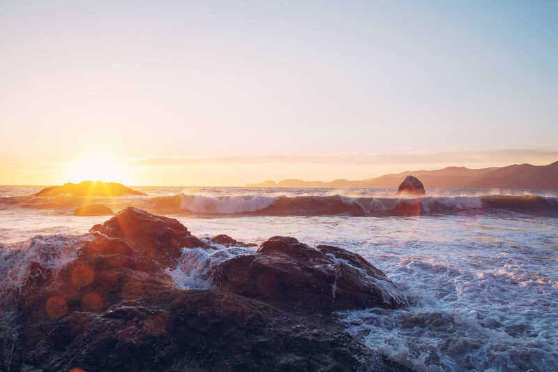 Sunset over waves breaking against a rocky shore