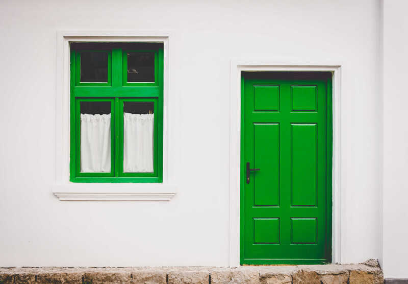 A green door and window on a white wall