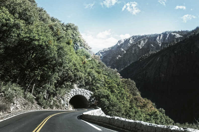 A mountain road curving toward a stone tunnel